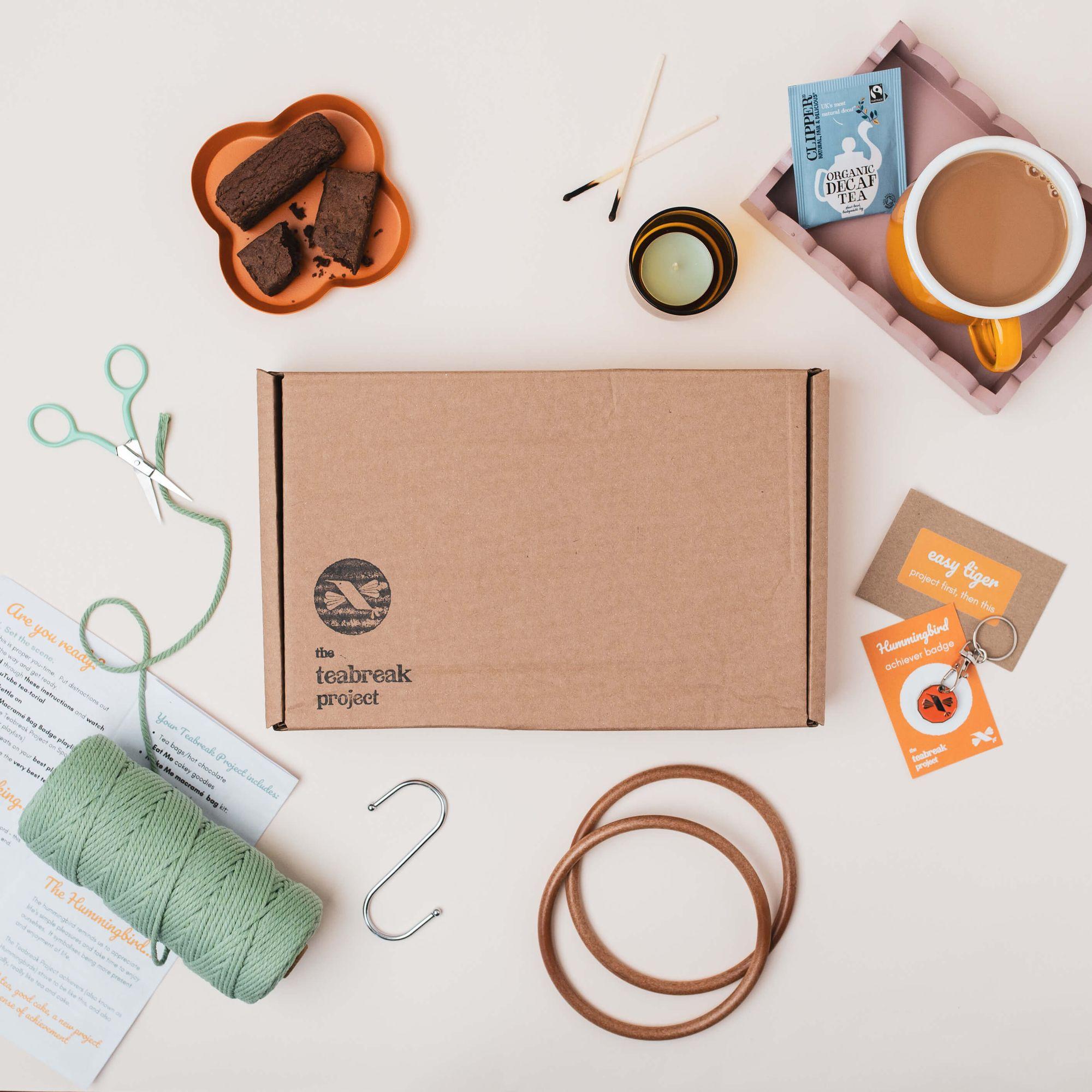 A Teabreak Project box surrounded by macramé cord, scissors, brownies, a lit tealight, tea and a Hummingbird achiever keyring