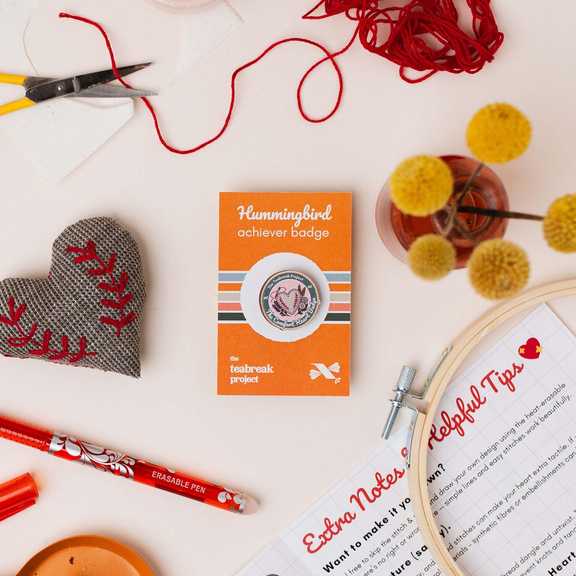Pressed flowers arranged on paper with washi tape, a Hummingbird achiever badge and a herbal tea sachet