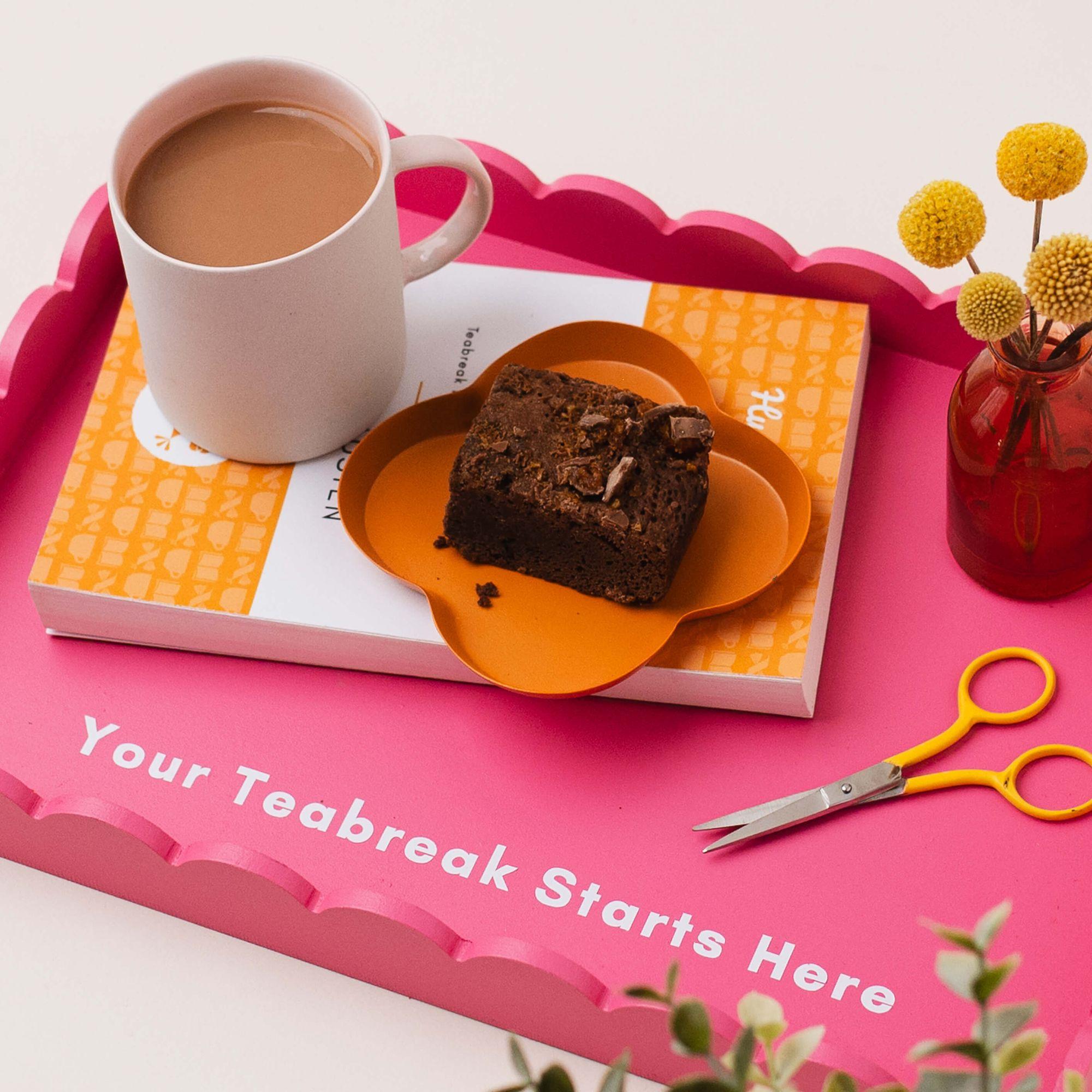 A mug of tea and a chocolate brownie on a flower-shaped plate, arranged on a Teabreak starter kit